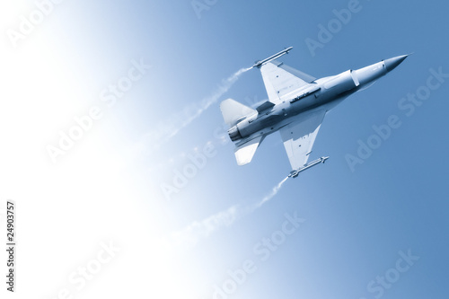 Fotografie military fighter jet flying through a gradient blue sky