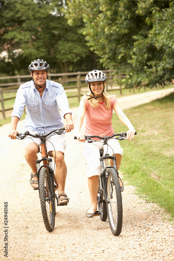 Couple Cycling In Countryside Wearing Safety Helmets Couple Cycling In Countryside Wearing Safety Helmets