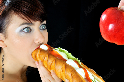Portrait of beautiful hungry girl eating sandwich looking at app