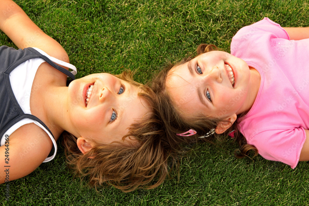 Two smiling girl lying on the grass - obrazy, fototapety, plakaty 