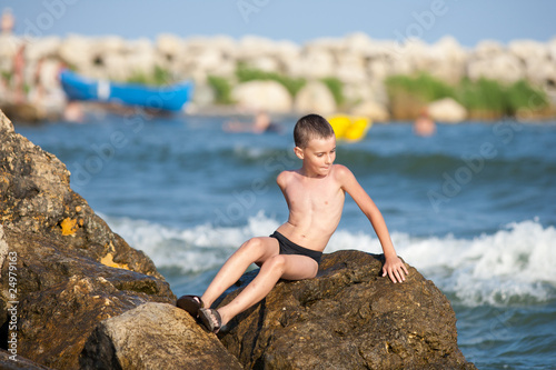 Little boy sitting on rocks at sea