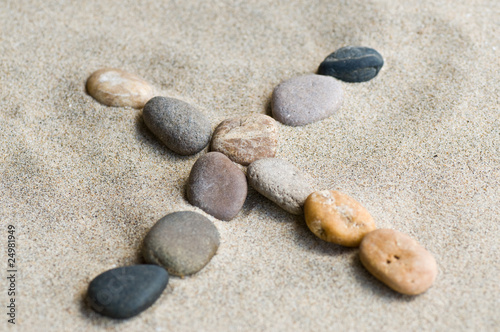lettre X en galets zen dans le sable