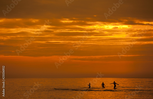Rodzina kąpiąca się w morzu podczas zachodu słońca © sitriel