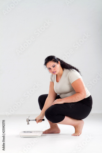 Foto unhappy overweight woman hitting scale with hammer