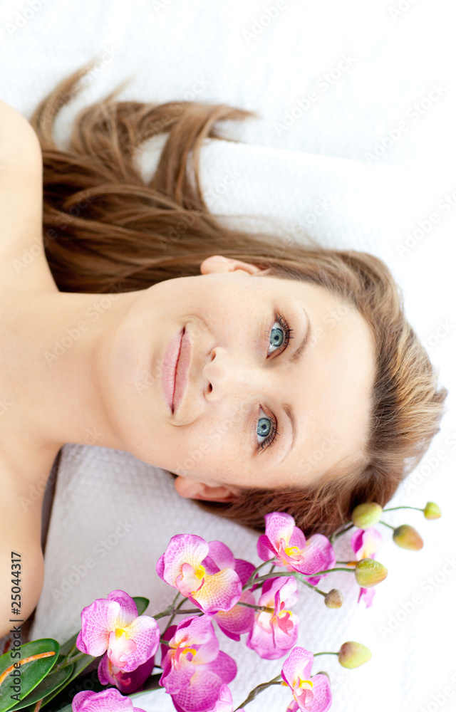 Captivating young woman lying on a massage table with flowers Captivating young woman lying on a massage table with flowers