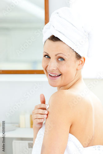 Delighted young woman putting cream on her body looking at the c