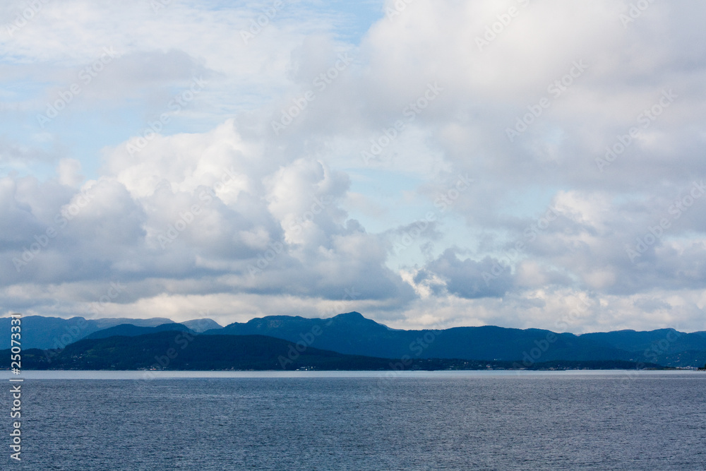 panorama with the sea, blue mountains and clouds with a blue sky in a mysterious summer day in Norway