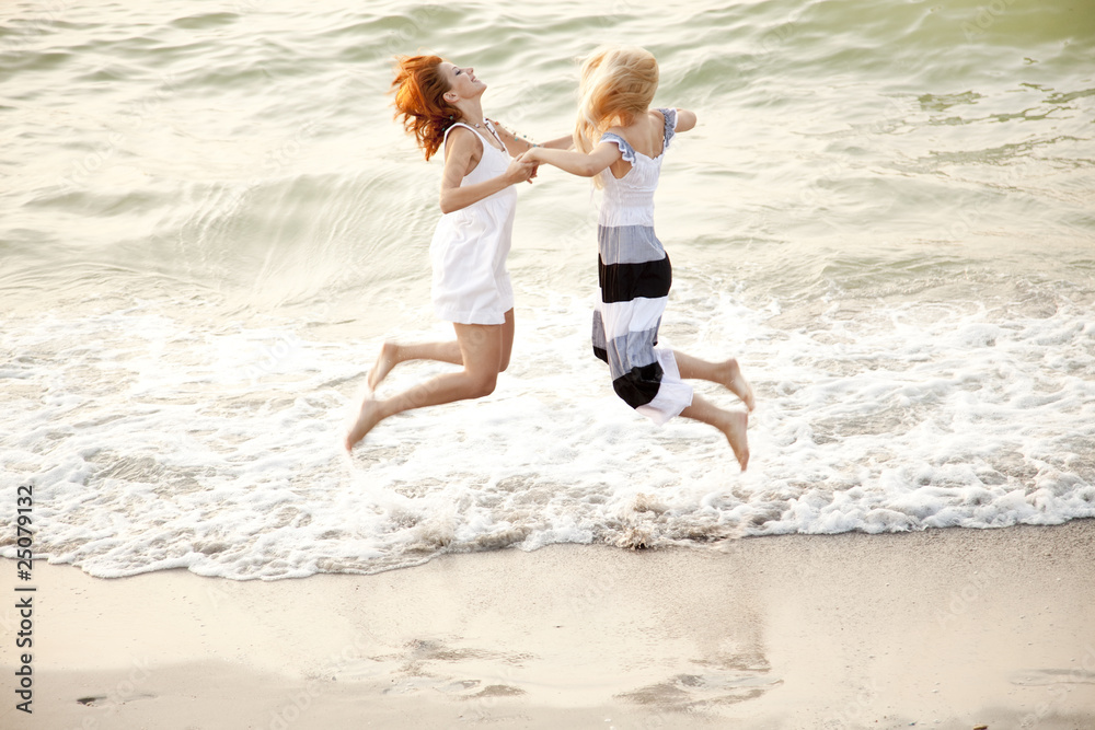 Fototapeta premium Two beautiful young girlfriends jumping on the beach
