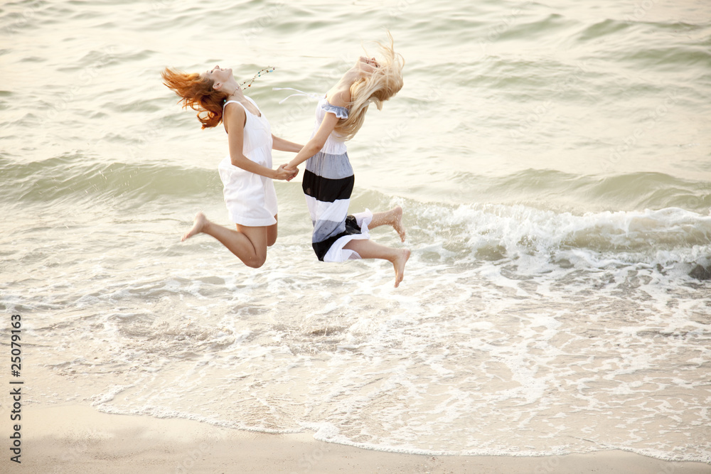 Fototapeta premium Two beautiful young girlfriends jumping on the beach