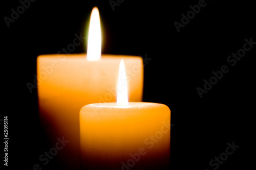 Close up of two lit white candles on black background.