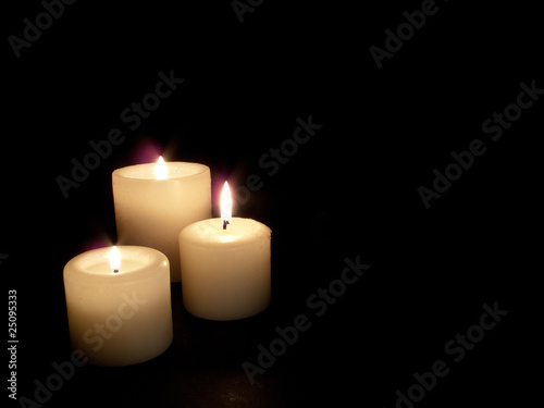 Close up of three lit candles on black background.