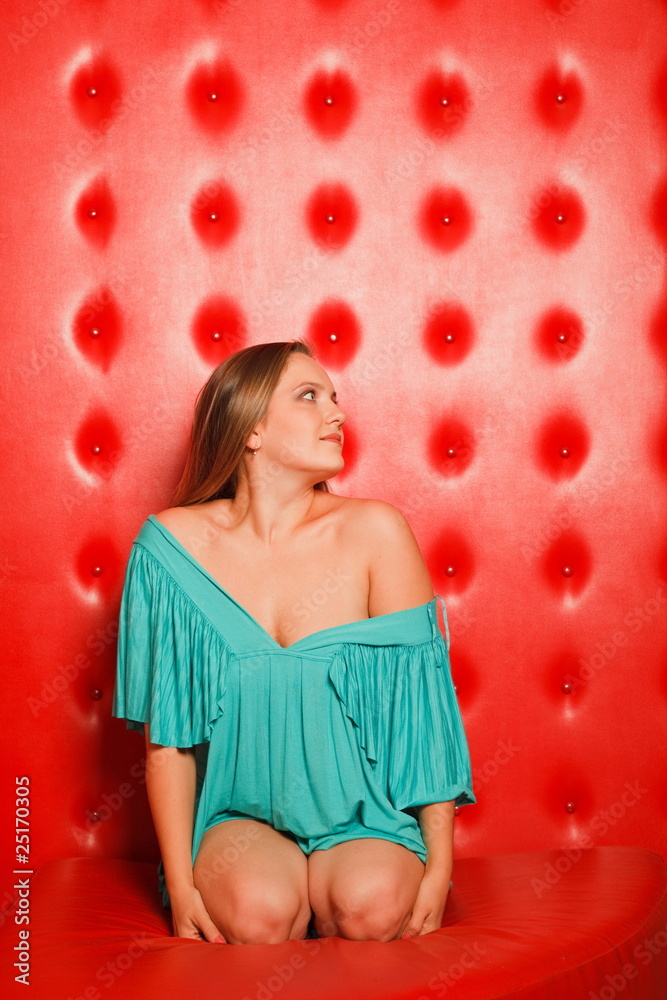 woman in a turquoise dress sitting on red leather couch woman in a turquoise dress sitting on red leather couch