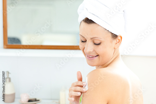 Attractive young woman with a towel putting cream on her face in