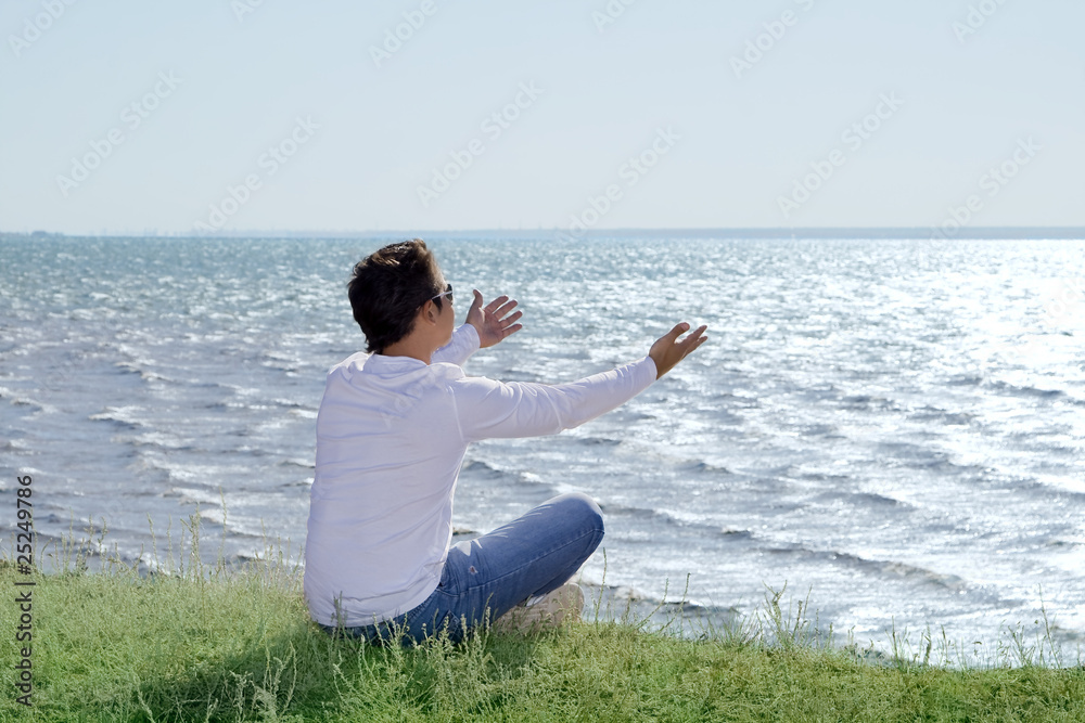 young man  sitting at precipice and looking on the sea shore