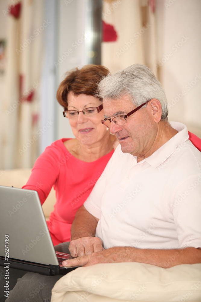 Senior couple sitting in sofa with laptop computer