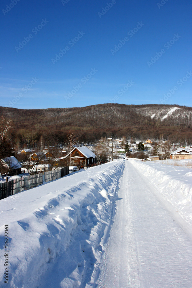 Winter village road against mountains and a blue sky