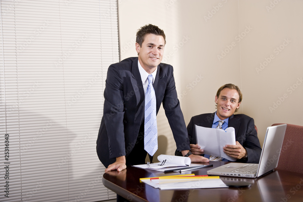 Two businessmen in suits working together in boardroom Two businessmen in suits working together in boardroom