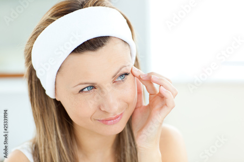 Fototapeta Pretty woman putting cream on her face wearing a headband in the