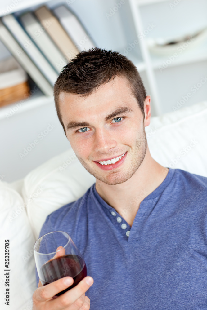 Charismatic young man holding a glass of wine sitting on a sofa Charismatic young man holding a glass of wine sitting on a sofa