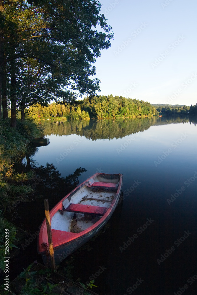 Obraz premium Evening summer countryside with pond, boat, forest and blue sky