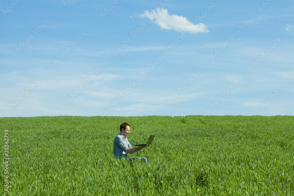 young man using laptop in the field young man using laptop in the field