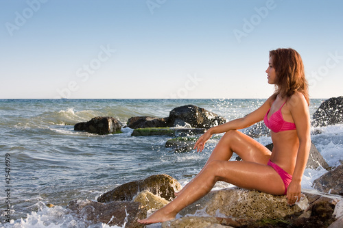 A young girl on the background of the sea sits on a rock