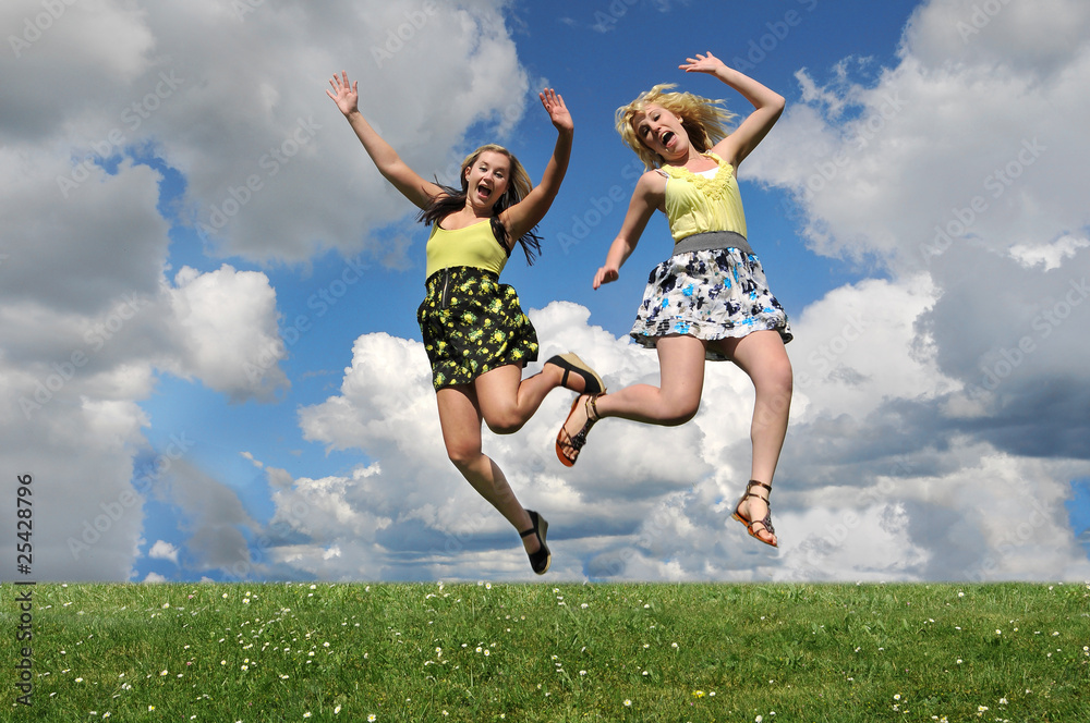 Two girls jumping over grass hill Two girls jumping over grass hill