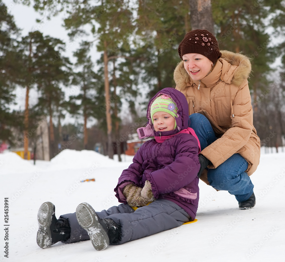 child sliding in the snow with  her mother