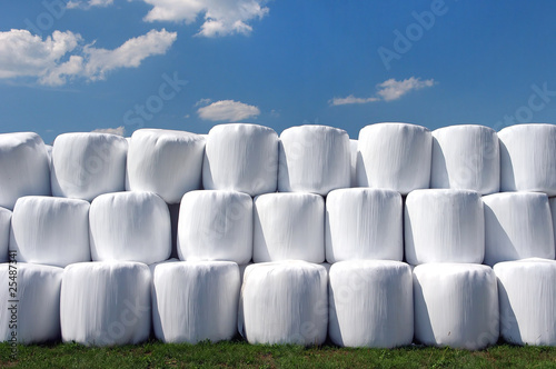 Countryside field with hay bale wrapped in plastic on sunny day