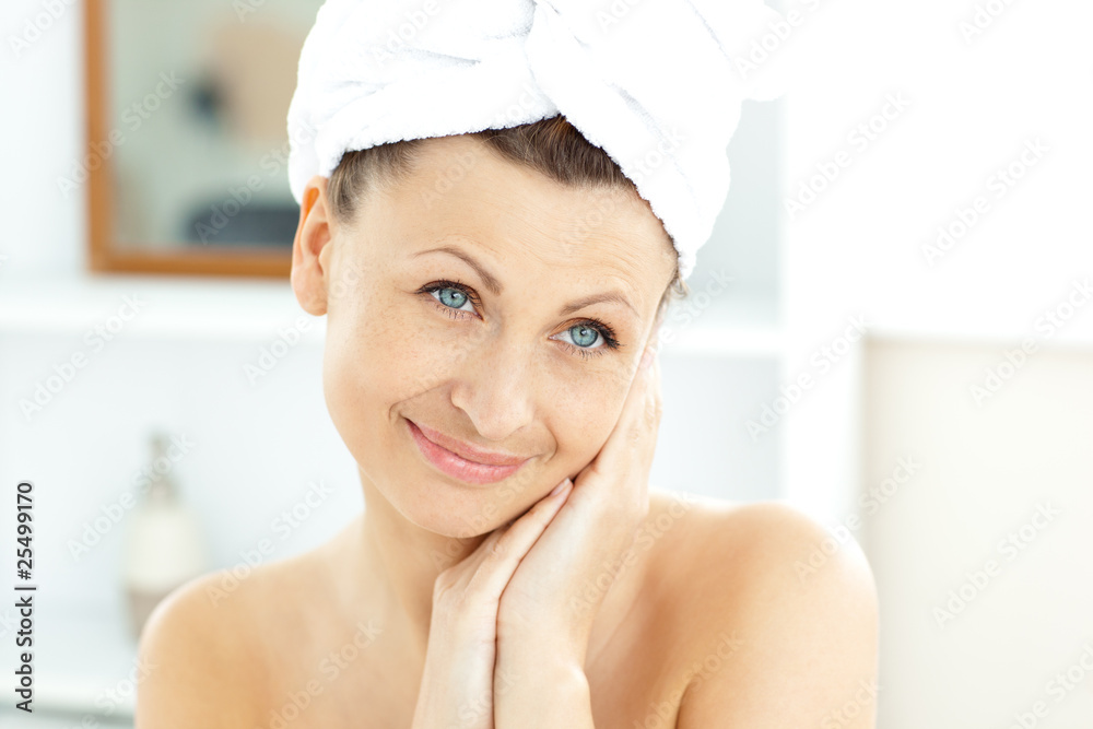 Radiant young woman with a towel putting cream on her face in th Radiant young woman with a towel putting cream on her face in th