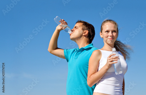 young couple with bottles of water against blue sky