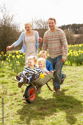 Father Giving Children Ride In Wheelbarrow Through Field Of Spri