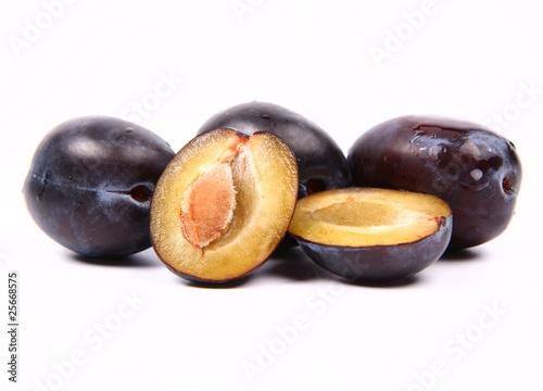 Plums on white background - one cut in half with a pit visible