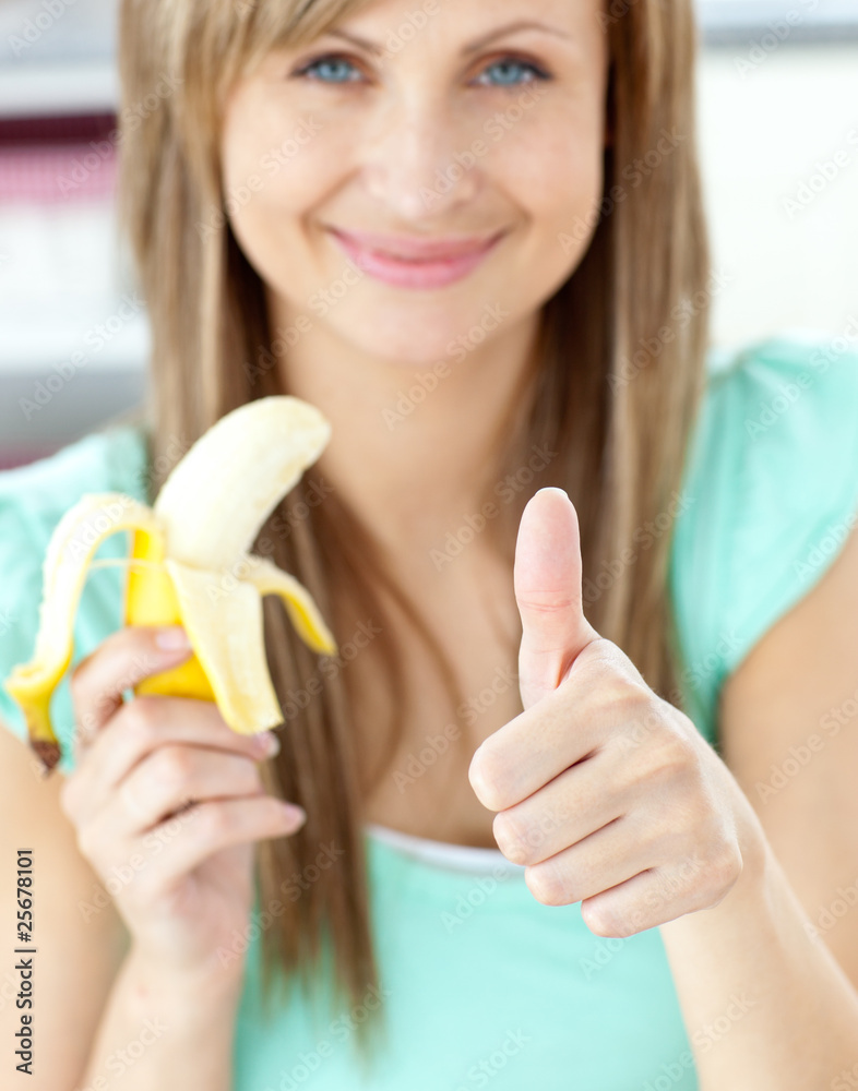 Smiling woman with thumb up holding a banana in the kitchen Smiling woman with thumb up holding a banana in the kitchen