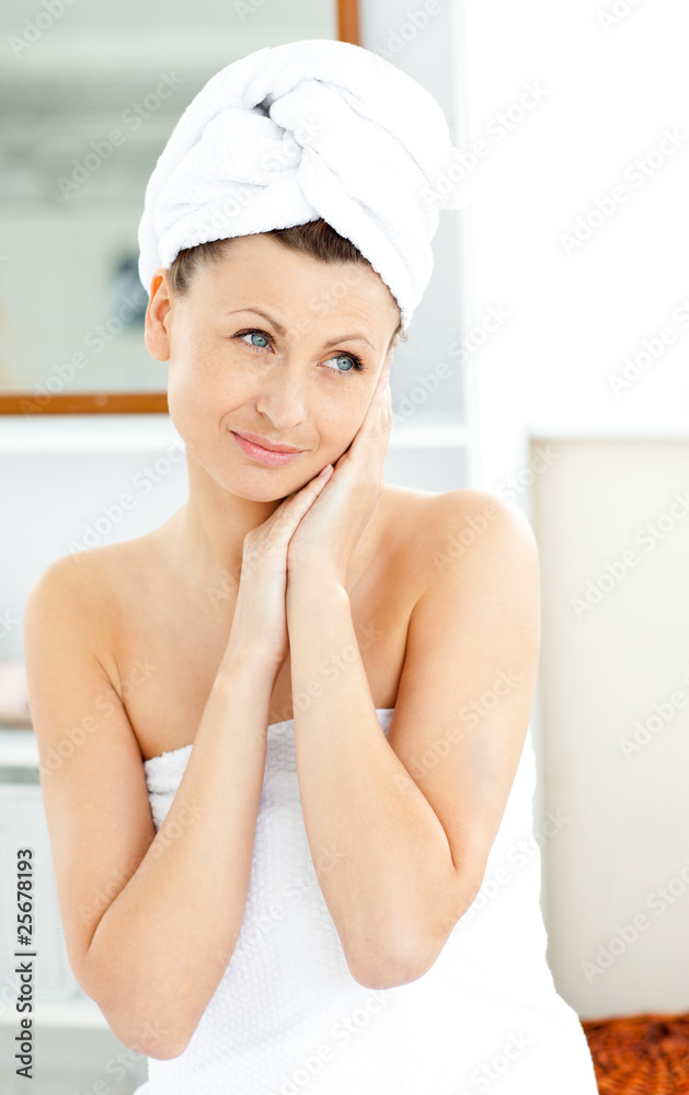 Charming young woman with a towel putting cream on her face in t Charming young woman with a towel putting cream on her face in t