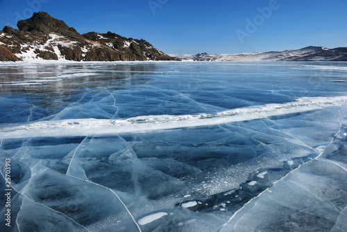 Surface of transparent fissured black ice of frozen lake