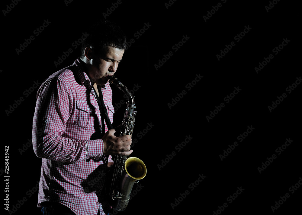 Fototapeta premium Young handsome man playing music on saxophone. black background