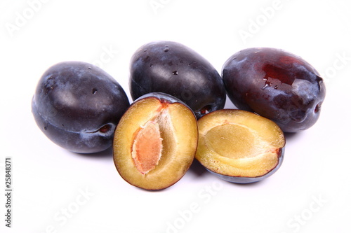 Plums on white background - one cut in half with a pit visible
