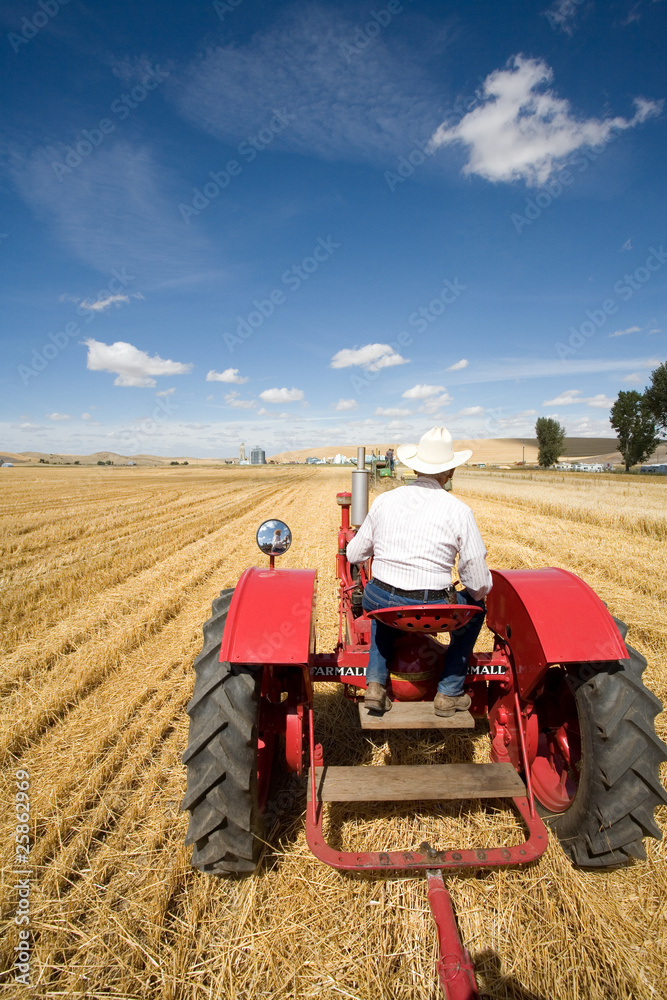 Obraz premium A man in a cowboy hat drives a tractor in a field.