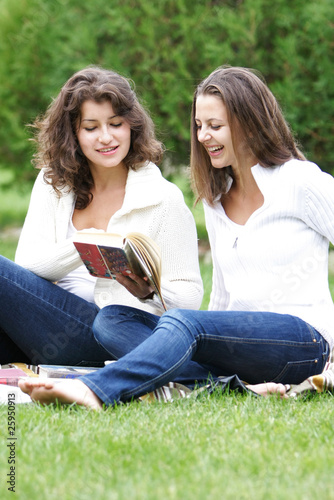two young girls reading book outdoors