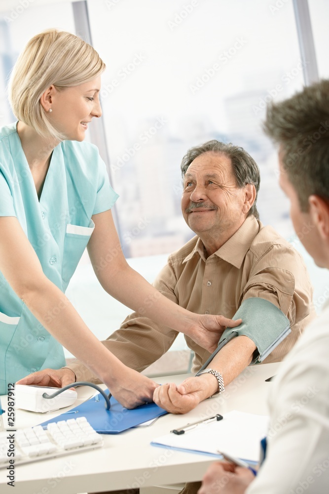 Obraz premium Smiling nurse measuring blood pressure of patient