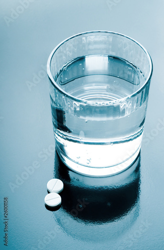aspirin pills and glass of water on glossy background