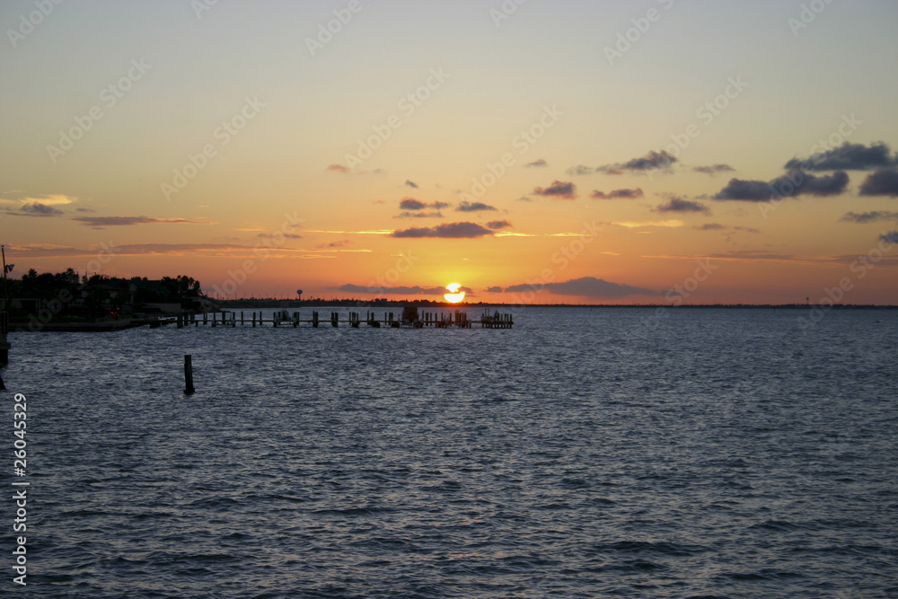 Golden glow of sunset on an ocean bay behind pier