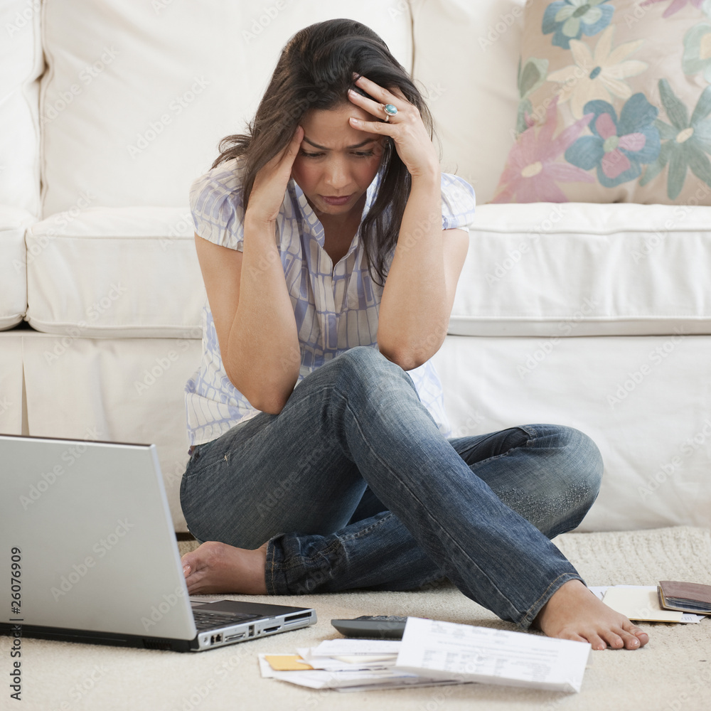 Hispanic woman looking at bills with head in hands Hispanic woman looking at bills with head in hands