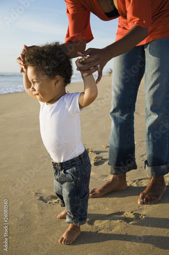 African mother helping son walk in beach
