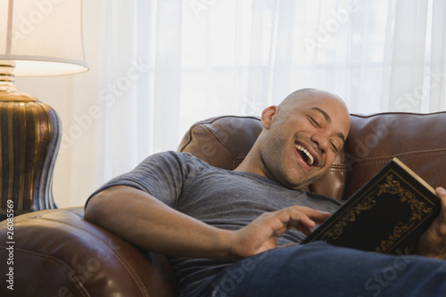 Mixed race man in armchair reading book photo