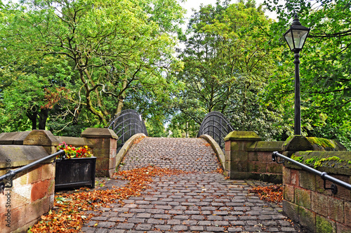 Crossing the old bridge amongst the trees via a traditional cobbled footpath  in the pretty village of Worsley near Manchester photo