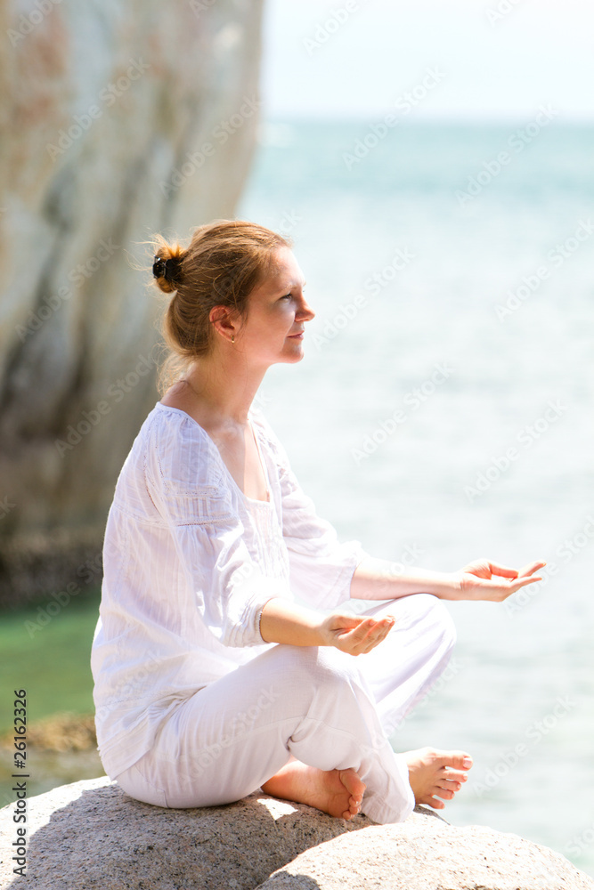 Young woman practicing yoga by coast