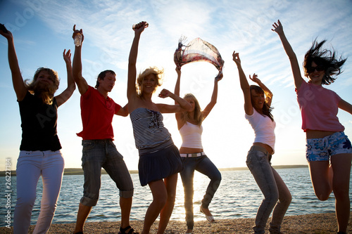 group of happy young people dancing at the beach
