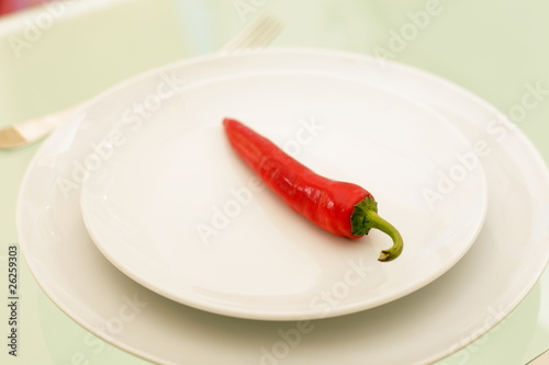 one red chili served on a plate with knife and fork and spoon